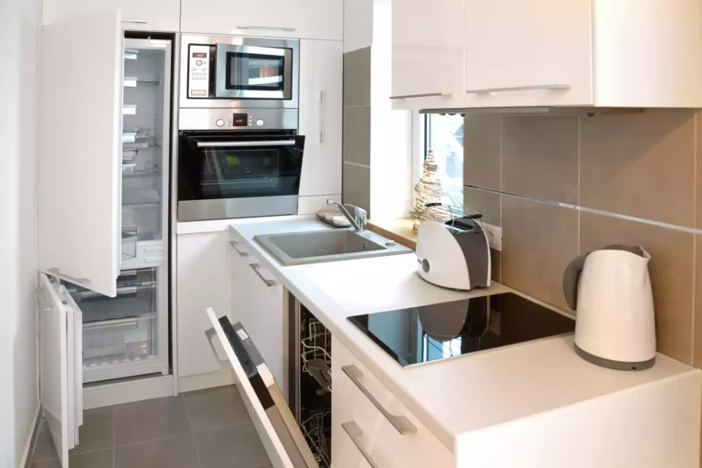 A small kitchen with white cabinets, counters and appliances. The fridge, oven and microwave doors are open.