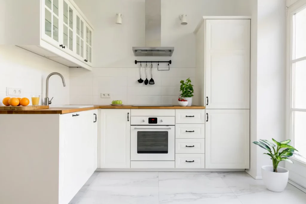 Creative Kitchen Storage Ideas. Silver cooker hood in minimal white kitchen interior with plant on wooden counter top